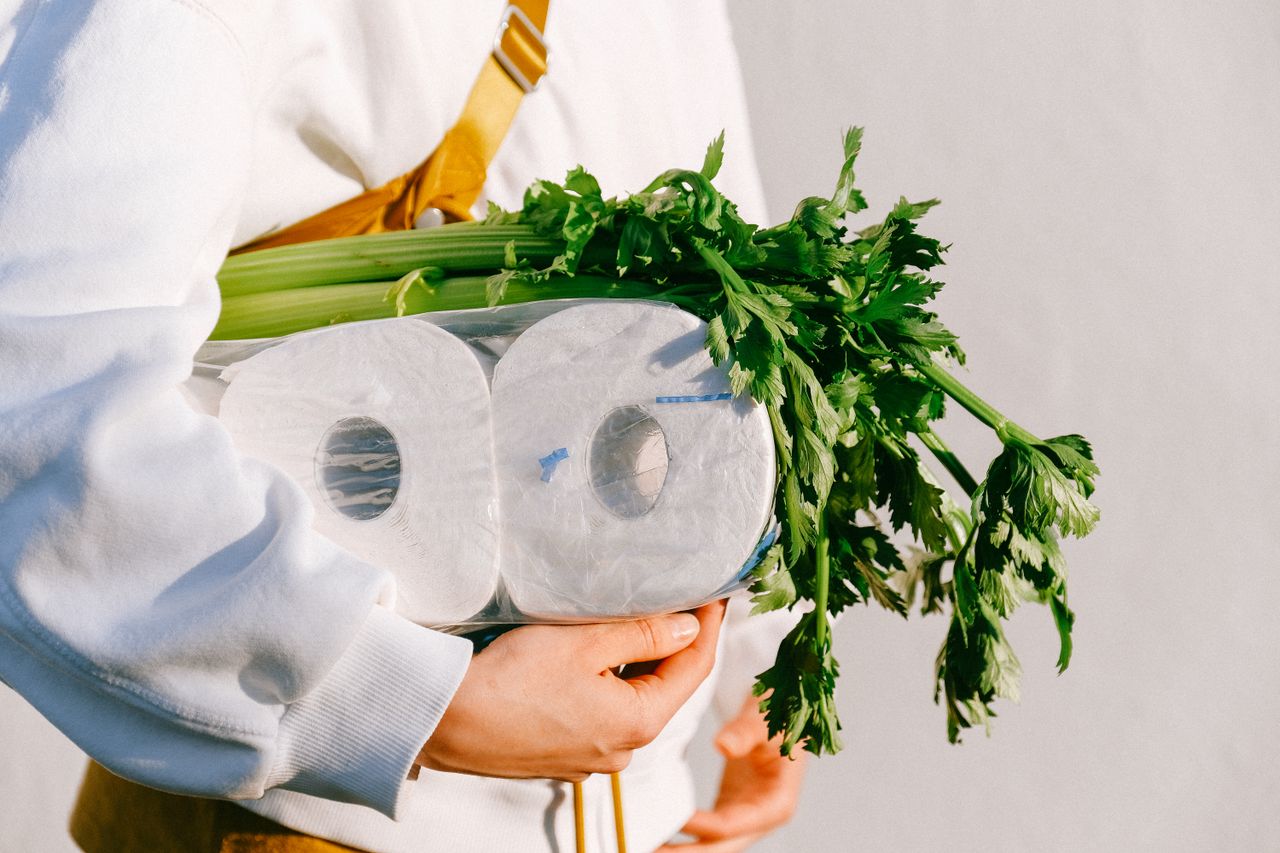 Close-up of hands holding toilet paper and celery stalks, emphasizing daily essentials.