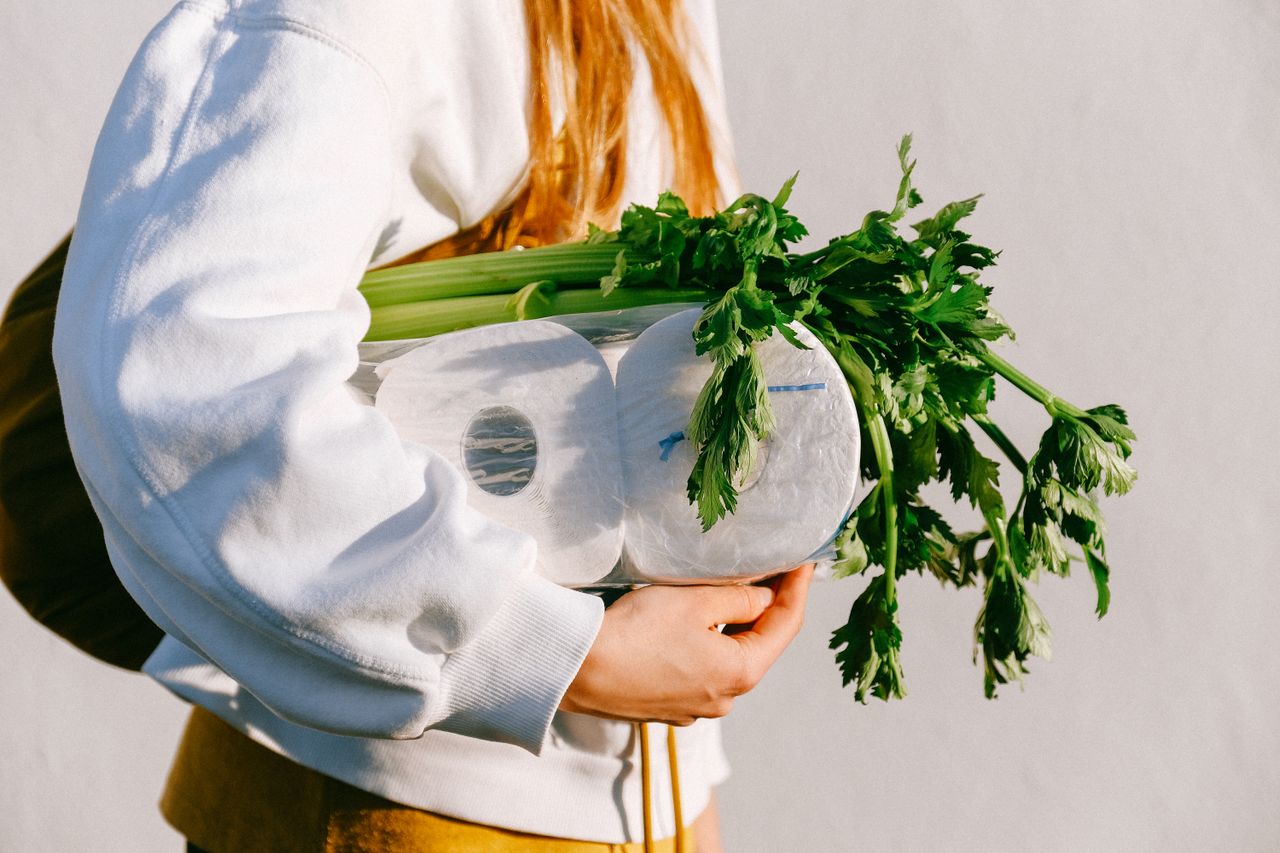 Close-up of someone holding celery and rolls of toilet paper outdoors.
